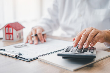 Wall Mural -  woman calculates her budget before signing a real estate project contract with a house model.