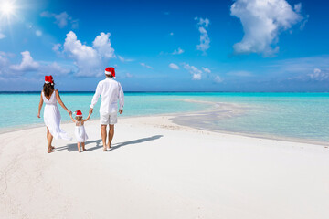 Wall Mural - A beautiful family in white summer clothes and with santa claus hats walks down a tropical paradise beach during their christmas holidays