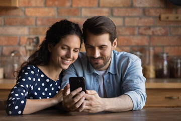 Wall Mural - couple use smartphone. loving young husband wife sit at table close together embrace watch video on 