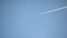High Flying Airplane Jet Leaves A Contrail. Plane Fly Against Blue Cloudless Sky Leaving Water Vapor Contrails Behind As Seen From The Ground. Aircraft Passing By. Real Time, Static Shot