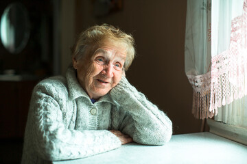 Wall Mural - An old woman sits in the her house near the window.