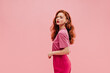 © Look! - Cute caucasian young girl with fluffy wavy hair on one side on pink background with place for text. Red-haired lady in wide T-shirt and crimson pants looks at camera with her mouth open.