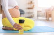 Young pregnant woman in stylish sportswear with bottle of water at home