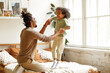 © JenkoAtaman - Happy african american father and son jumping on bed and laughing while playing together at home