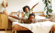 Happy African American Family Father And Son In Flying Pose Lying On Bed At Home