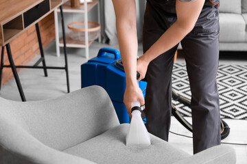 Wall Mural - Male worker removing dirt from grey armchair with vacuum cleaner in room