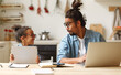© JenkoAtaman - Young african american father works remotely on laptop while his little son using digital tablet