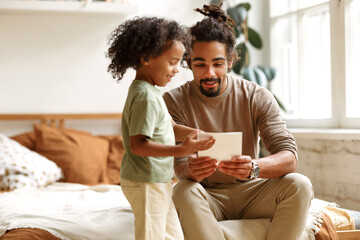 Cute little boy son giving handmade greeting card with hand drawn heart to dad