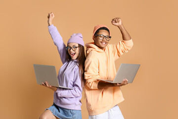 Wall Mural - Happy young couple in hoodies with laptops on beige background