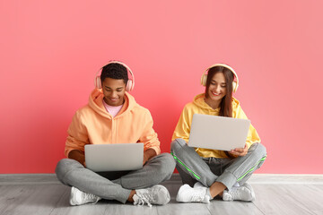 Wall Mural - Stylish young couple in hoodies using laptops near pink wall