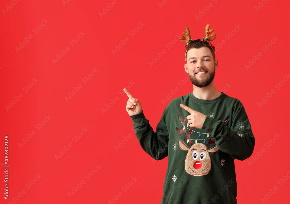 Young man in stylish Christmas clothes showing something on color background