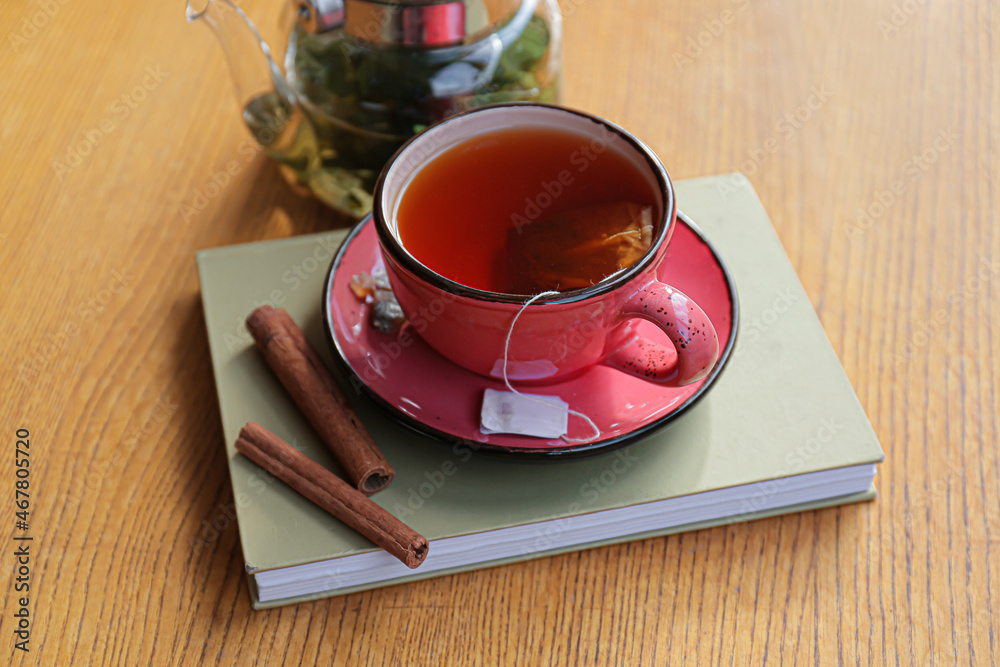 Cup of hot tea, book and cinnamon on wooden table