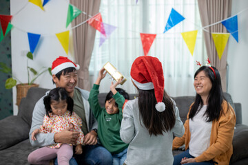 Asian Happy family with daughter in Santa hats gathered together on Christmas time and enjoy gifts box