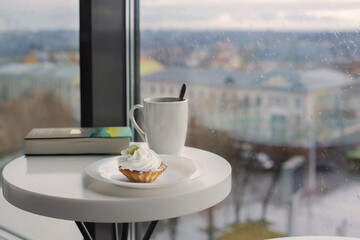 Wall Mural - cupcake with cup on white table near window in cafe