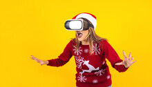 Young Latin Woman Gamer In Virtual Reality Headset Gadget Wearing Santa Hat And Christmas Sweater On Yellow Background. Christmas And Winter Vr Technology Concept In Mexico Latin America