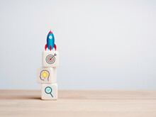 Business Startup With Growth Success Process For Leadership Concept. The Rocket Beside The White Cube Blocks Stacks With Business Strategy Icons On Wooden Table On White Background With Copy Space.