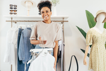 Wall Mural - Cheerful woman working in clothing store holding a bunch of hangers