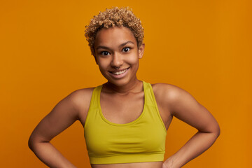 Wall Mural - Attractive young athletic female with small blonde poodles and nose piercing posing against orange studio wall with surprised face expression, looking at camera with amazed smile, feeling astonished