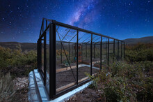 Glass Greenhouse In The Middle Of A Shrubland Under The Starry Composite Milky Way Sky