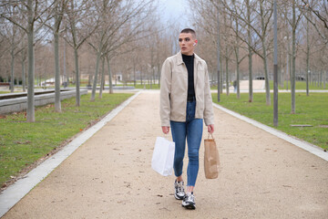 Wall Mural - Young man wearing make up walking with shopping bags and listening music.