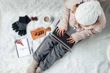 Poster - A girl with winter clothes working with laptop at home and enjoying winter season with hot chocolate and cookies