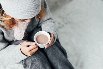 Wall Mural - A girl with winter clothes enjoying a cup of hot chocolate on winter season at home