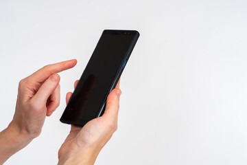 Poster - Phone in female hands. Smartphone in hand close up. Girl points her finger at screen. Mobile gadget on light background. Copy space on black screen of phone. Modern Cellphone with dark display