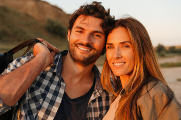 Wall Mural - Young white couple smiling and looking at sunset while walking