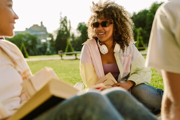 Multiracial young students smiling together while resting on grass