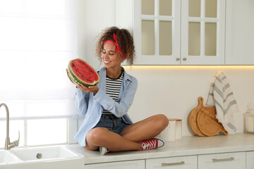 Canvas Print - Beautiful young African American woman with half of watermelon sitting on countertop in kitchen