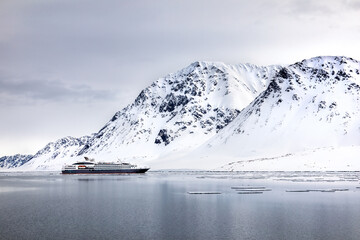 Wall Mural - pristine snow covered mountains of svalbard with tourist cruise ship in the fiord. ecotourism is bec
