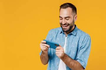 Poster - Gambling young happy man 20s wearing blue shirt white t-shirt using play racing app on mobile cell phone hold gadget smartphone for pc video games isolated on plain yellow background studio portrait