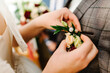 Bride's hands puts the groom on jacket a wedding boutonniere. Wedding concept.