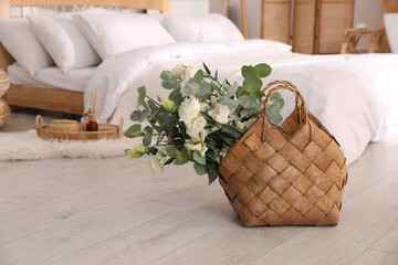 Wall Mural - Stylish wicker basket with fresh eucalyptus branches and flowers on floor in bedroom