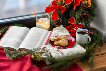 winter holidays and leisure concept - open book, fir branch, oatmeal cookies, cup of coffee and christmas decorations on window sill at home