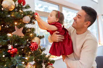 Poster - winter holidays and family concept - happy middle-aged father and baby daughter decorating christmas tree with ball at home