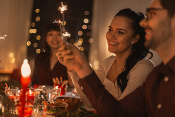 Poster - holidays and celebration concept - multiethnic group of happy friends with sparklers having christmas dinner at home