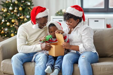 Wall Mural - family, winter holidays and people concept - happy african american mother, father and little son opening gift box with toy car at home on christmas