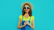 Summer portrait of happy smiling young woman with lollipop wearing a straw hat on blue background