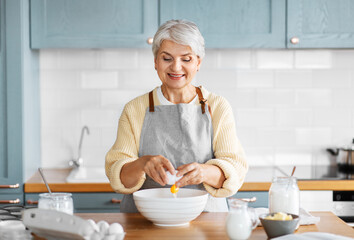 Canvas Print - people and culinary concept - happy smiling woman cooking food on kitchen at home and breaking egg