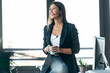 © nenetus - Elegant business woman talking with earphone while holding cup of coffee in modern startup office.