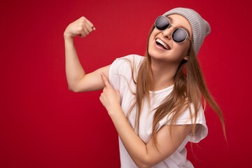 Wall Mural - Portrait photo of young emotional positive happy beautiful attractive dark blonde woman with sincere emotions wearing casual white t-shirt with empty space for mockup, grey hat and sunglasses isolated