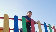 A Little Boy Jumps On The Bridge Of A Children's Castle On The Playground Against The Sky.