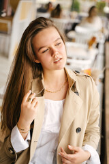 Wall Mural - A cute girl in a beige raincoat sits in a cafe and looks out the window