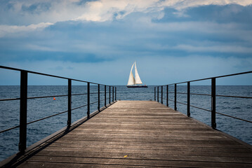 Wall Mural - Small empty wooden pier and a sailing boat in the horizon of the Mediterranean sea, Italy, Europe.