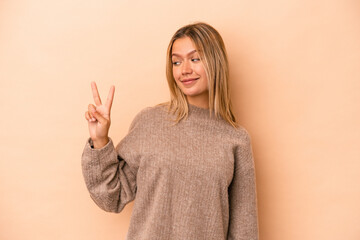 Poster - Young caucasian woman isolated on beige background joyful and carefree showing a peace symbol with fingers.