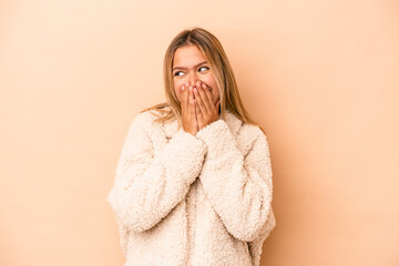 Wall Mural - Young caucasian woman isolated on beige background laughing about something, covering mouth with hands.