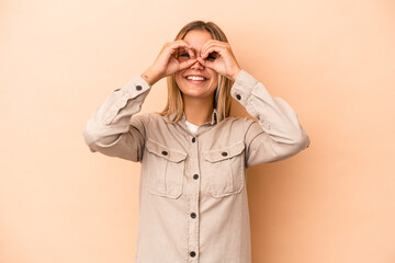 Wall Mural - Young caucasian woman isolated on beige background showing okay sign over eyes