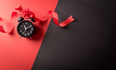 Wall Mural - Top view of Black Friday decoration made from alarm clock,  ribbon on red and black background. Shopping concept boxing day and Black Friday composition.