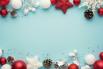 Top view photo of white and red christmas tree decorations disco balls stars snowflake pine cones snowy branches and sequins on isolated pastel blue background with copyspace